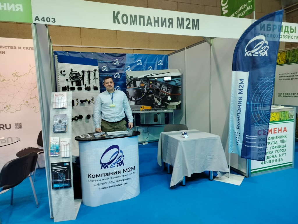 Стенд компании М2М на Агропромышленном форуме Сибири 2024. Демонстрация оборудования для мониторинга транспорта, ГЛОНАСС/GPS систем, тахографов и видеонаблюдения. Представитель компании у демонстрационного стенда с образцами оборудования.